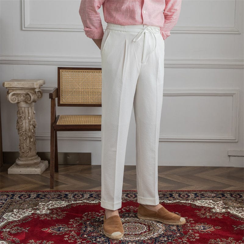 Man wearing white linen tailored pants with drawstring waist, standing on patterned rug indoors.